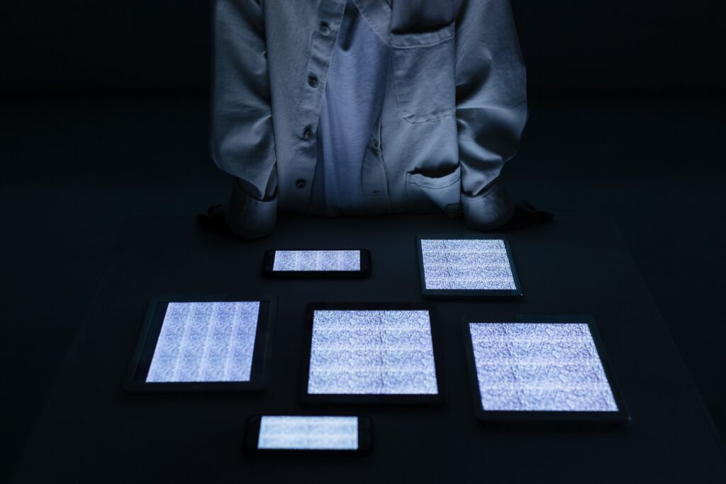 A person in a white shirt stands over tablets and phones with static screens in a dark room.